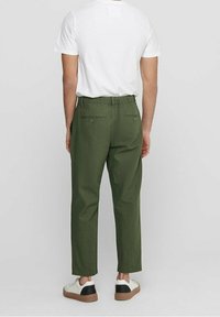 Donkergroene broeken met een relaxte fit, elastische tailleband en twee achterzakken, gecombineerd met een wit T-shirt met korte mouwen en sneakers.