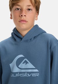 Blue hoodie made of soft fabric featuring a large white Quiksilver logo. It has a classic design with an adjustable drawstring hood.