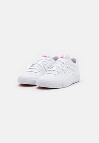 Des chaussures de sport blanches avec une tige en cuir lisse, des perforations, des lacets plats et une semelle en caoutchouc. Accents rouges sur la languette.