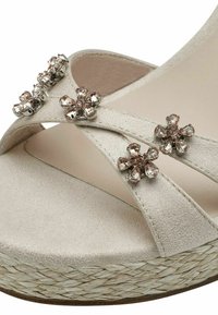 Beige πλατφόρμες διαθέτουν σχέδιο με σταυρωτές λωρίδες διακοσμημένο με λουλουδάτα στοιχεία και διάφανα ρόδια στρας; πλεγμένη σόλα από κολοβάκι, μαλακό ύφασμα στην επάνω πλευρά.