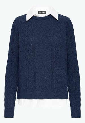 Tengerészkék kötött pulóver, texturált kábeldesignnal, alatta fehér galléros inggel. Hosszú ujjak és bordázott szegély zárja le.