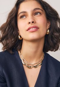 Gouden sieradenset bestaat uit een stevige ketting met schakels en oorringen. De ketting heeft gladde, gebogen schakels; de oorbellen zijn gepolijst met een afgerond ontwerp.