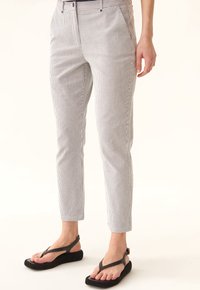 Pantalons légers à rayures verticales, avec une coupe slim et une longueur légèrement raccourcie. Associés à des sandales à talons compensés noires.