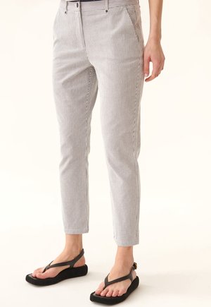 Pantalons légers à rayures verticales, avec une coupe slim et une longueur légèrement raccourcie. Associés à des sandales à talons compensés noires.