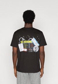 Μαύρο βαμβακερό T-shirt με γραφιστικό σχέδιο πίνακα αναχωρήσεων με πολύχρωμες πληροφορίες πτήσεων και κάρτες επιβίβασης.