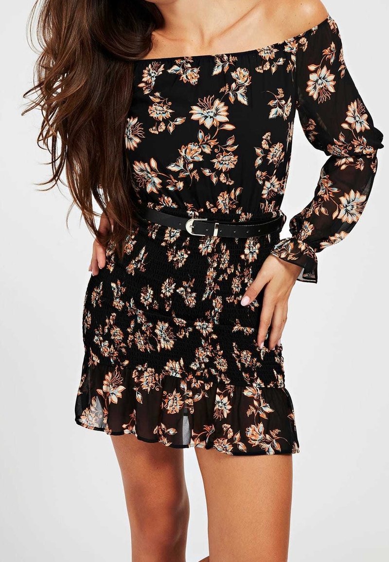 Robe noire décolletée avec des manches longues, ornée d'un motif floral orange et bleu, taille smockée et ourlet à volants. Accompagnée d'une ceinture noire.