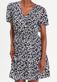 Robe à motifs bleu marine et crème avec un décolleté en V, des manches courtes et une taille élastique, présentant des formes géométriques et une jupe évasée.