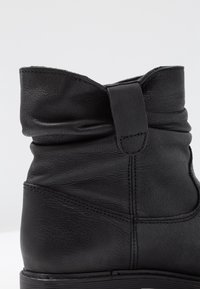 Czarne skórzane buty z obniżonym fasonem, zaokrąglonym noskiem i ozdobnym paskiem z tyłu. Gładka faktura i delikatne przeszycia.