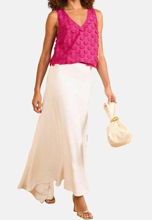 Mujer que lleva una blusa rosa sin mangas con textura, falda larga fluida color crema, sandalias doradas y sostiene un bolso crema con asa anilla dorada.