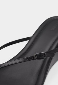 Μαύρο δερμάτινο σανδάλι με λεπτό ρυθμιζόμενο λουράκι και μικρή μεταλλική αγκράφα σε ομαλή σόλα.