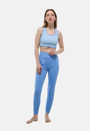Brassière de sport bleu clair avec détails en mesh et leggings assortis bleus. Le tissu est extensible et ajusté, créant une silhouette élégante.