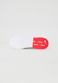 Sola de sapatilha atlética branca e vermelha com padrões de aderência texturizados; seção do calcanhar vermelha com canais de drenagem distintos; design minimalista.