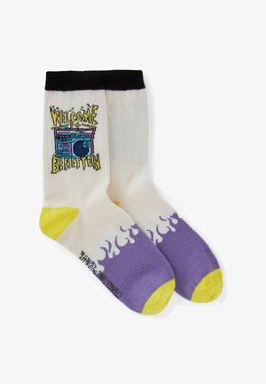 Weiße Sportsocken mit schwarzem Bündchen, gelber Ferse und Spitze, lila Flammenmuster an den Füßen und dem Text "WELCOME TO BANETTOW" mit einem Retro-Arcade-Grafikdesign.