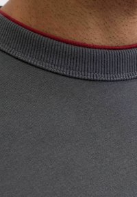 Zbliżenie szarego materiału z prążkowanym dekoltem, ozdobionym kontrastującym akcentem w kolorze bordowym. Teksturalny, elastyczny materiał o gładkiej powierzchni.