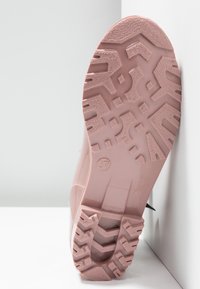 Semelle d'une chaussure rose avec des motifs de crampons profonds et la taille numéro 37, positionnée debout contre une surface blanche.