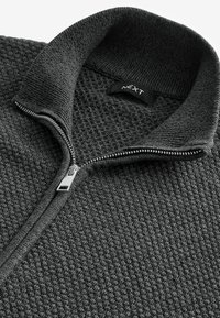 Dunkelgrauer Fleece-Reißverschluss-Pullover mit strukturiertem Muster. Verfügt über einen hohen Kragen, einen silbernen Reißverschluss und ein Markenlabel auf der Innenseite.