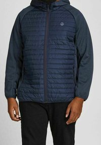 Mörkblå puffjacka med huva, med quiltade frampaneler och släta ärmar. Dragkedjestängning och sidofickor. Lättviktig design.