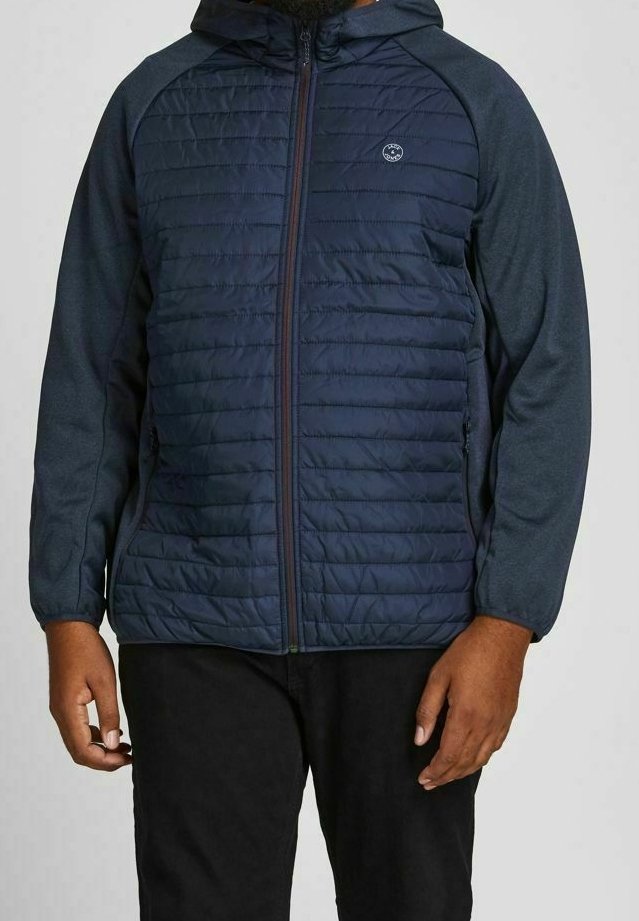 Mörkblå puffjacka med huva, med quiltade frampaneler och släta ärmar. Dragkedjestängning och sidofickor. Lättviktig design.