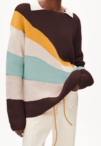 Pull en tricot avec un large col, présentant des rayures ondulées en marron, crème, jaune et bleu sarcelle, avec une texture côtelée et un col blanc.