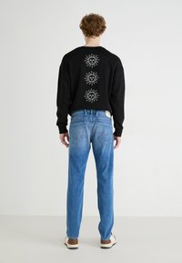 Black sweatshirt with three white sun designs on the back, paired with light blue denim jeans featuring a straight-leg cut and two back pockets.