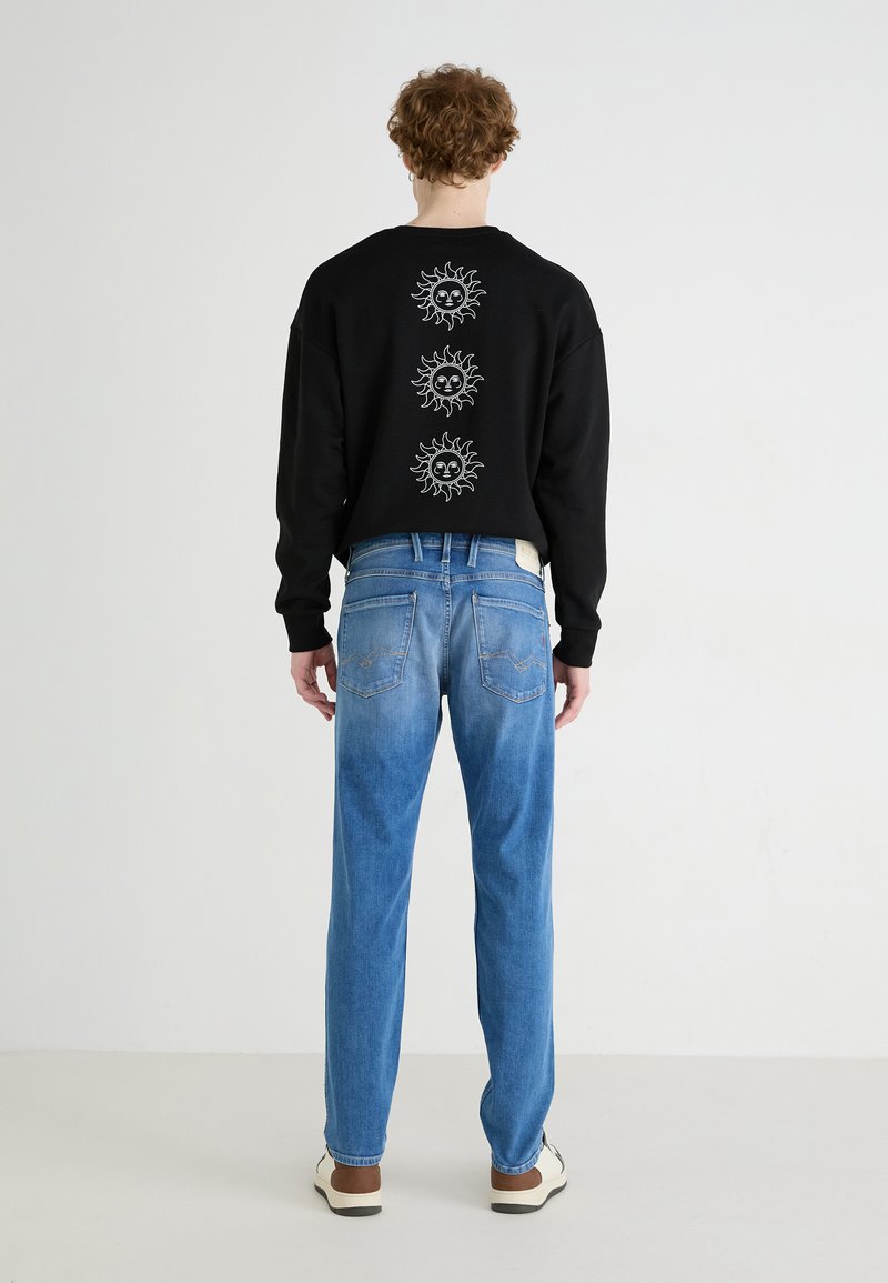 Black sweatshirt with three white sun designs on the back, paired with light blue denim jeans featuring a straight-leg cut and two back pockets.