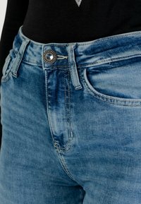 Jeans in denim blu con un lavaggio chiaro, dotati di chiusura con bottone in argento e un semplice design della tasca anteriore. Il tessuto ha una consistenza morbida e consumata.