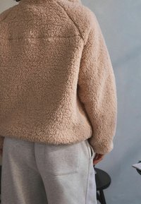 Pink, blød fleecepullover med en tekstureret overflade, kombineret med grå joggingbukser. Har en afslappet pasform og minimal syningsdetalje.