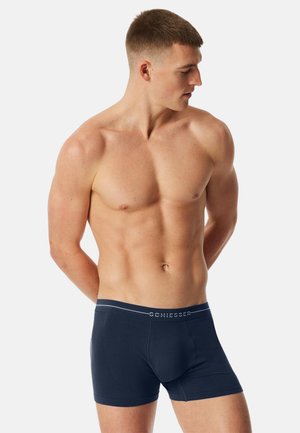 Marineblaue Boxershorts aus weichem Stoff, mit einem figurbetonten Schnitt, einem mit Logo versehenen Bund und einer glatten Textur, Seitenprofil sichtbar.