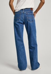 Sinine denim laiad püksid kõrge vöökohaga, tagakotidega, nahast sildiga vööl ja kergelt pleekinud tekstuuriga.