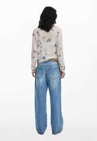 Leichter, cremefarbener Pullover mit Blumenmustern, kombiniert mit lockeren, hellblauen Jeans mit hoher Taille und großen Taschen.