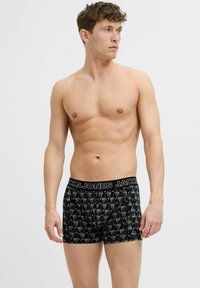 Black boxer shorts with a patterned design, featuring white cartoon faces, and a black elastic waistband with "JACK & JONES" in white lettering.