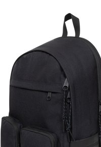 Czarny plecak o gładkiej fakturze, zaokrąglonym kształcie, podwójnych kieszeniach na zamek oraz górnym uchwycie do noszenia. Posiada trwały materiał i minimalistyczny design.