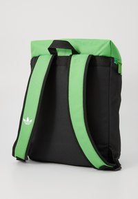 Zaino con corpo nero e accenti verde brillante, dotato di spallacci verdi imbottiti e chiusura con zip nella parte superiore.