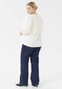 Kermakraft blouse gyda llewys puff a manylion lace ar y mwclis, wedi'i chyfuno â jeans glân las a esgidiau uchel du.