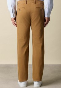 Beige Baumwollhosen mit geradem Schnitt, ausgestattet mit zwei Gesäßtaschen und dezenten Nähten. Kombiniert mit weißen Sneakern.