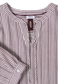 Chemise à manches longues rayée en blanc et bordeaux avec col rond et poignets boutonnés, affichant des étiquettes de marque cousues à l'intérieur du col.