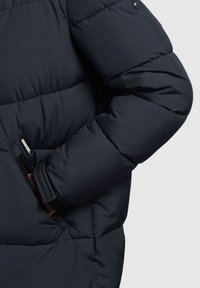 Marineblaue Steppjacke mit einem Reißverschlusstaschen, gestepptem Muster und eng anliegenden Bündchen, die für Wärme stark gepolstert ist.