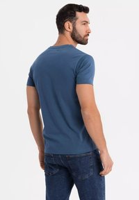 Camiseta de hombre de manga corta en azul suave, hecha de tela suave, con cuello redondo y diseño ajustado, combinada con jeans oscuros.