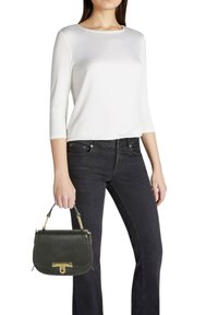 Jeans neri, top bianco a maniche tre quarti, con in mano una piccola borsa in pelle verde scuro con dettagli dorati e forma strutturata.