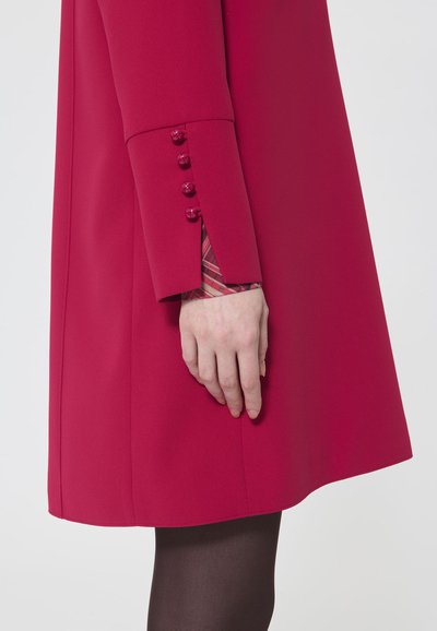 Fuksjowy płaszcz z teksturowanej tkaniny, charakteryzujący się eleganckim krojem, dopasowanym rękawem z guzikowymi akcentami oraz kontrastową, kratkowaną podszewką.