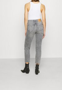 Šedé vysoké džíny s rovnými nohavicemi, roztrhaným lemem, pěti kapsami a béžovou koženou nášivkou na zadní straně. Skombinováno s černými kotníkovými botami.