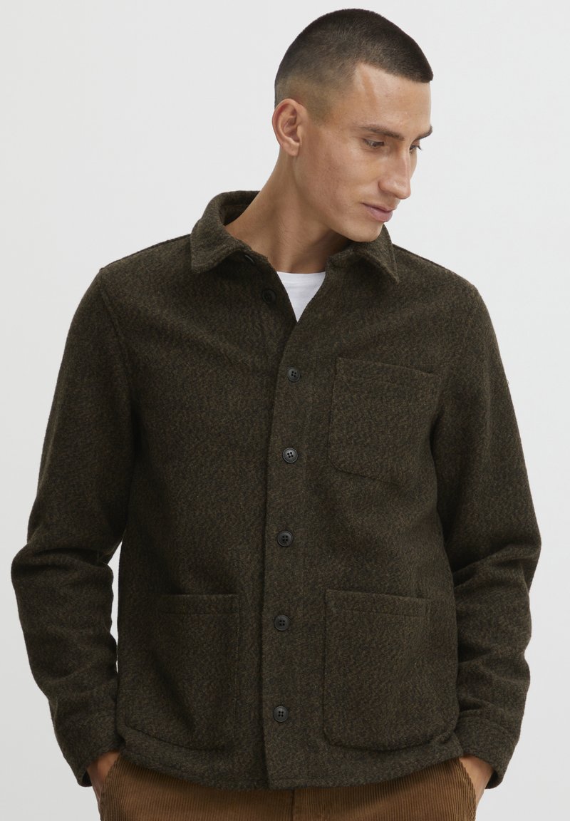 Camisa chaqueta mezcla de lana en verde oscuro, con cierre de botones, cuello extendido y dos bolsillos delanteros de parche con un patrón texturizado.