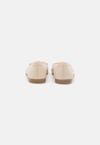Scarpe slip-on beige in pelle con punta arrotondata, dettagli di cucitura minimi e suola in gomma marrone.