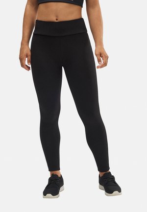 Leggings negros de talle alto, hechos de material elástico, con una textura suave y un diseño ajustado, combinados con zapatillas deportivas negras.
