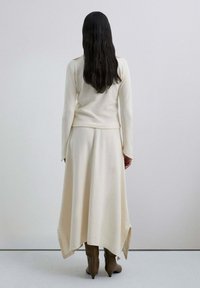 Maglione lavorato a maglia color crema con maniche lunghe abbinato a una gonna fluida lunga fino alla caviglia. Presenta delle fessure laterali ed è indossato con stivali al ginocchio con punta acuminata.