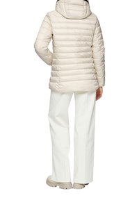 Hellbeige, gesteppte Pufferjacke mit Kapuze, die eine glatte Textur und eine taillierte Passform aufweist. Kombiniert mit weit geschnittenen weißen Hosen und beigen Schuhen.