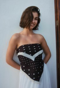 Czarny i biały top bez ramiączek w groszki z wzorem w jodełkę i białymi lamówkami, wykonany z lekkiego materiału. Gładka faktura, dopasowany krój.