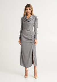 Abito grigio a maniche lunghe con collo a cascata, lati arricciati e uno spacco laterale. Realizzato in un tessuto liscio con una silhouette aderente.