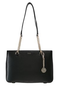 Sac à main en cuir noir rectangulaire avec des poignées en chaîne dorée et un charme en forme de logo circulaire DKNY suspendu sur le côté droit à l'avant.