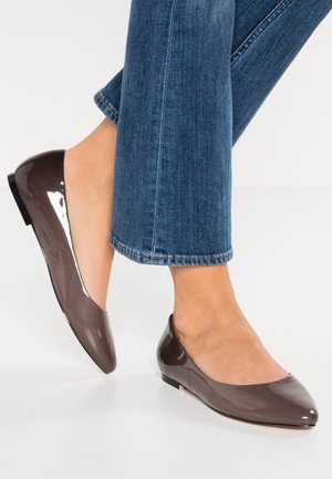 Brązowe baleriny z lakierowanej skóry z zaokrąglonym noskiem i niskim obcasem, zestawione z niebieskimi dzwonowatymi dżinsami. Gładka, błyszcząca faktura.